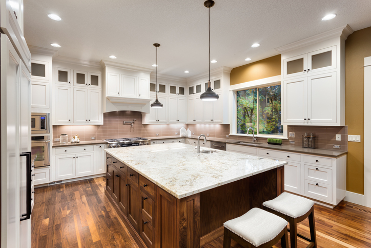 Modern kitchen with a mix of light and dark granite countertops, featuring a central island with a light speckled surface and dark wood base, surrounded by white cabinetry and stainless steel appliances.