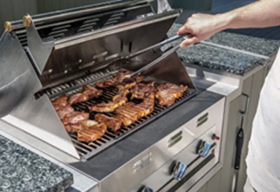 A man grilling chicken on a barbecue built into a granite countertop in an outdoor kitchen.