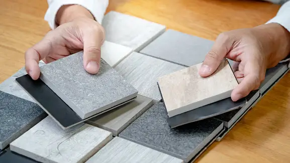Hands selecting from a variety of natural stone countertop samples, showcasing texture, color, and finish options