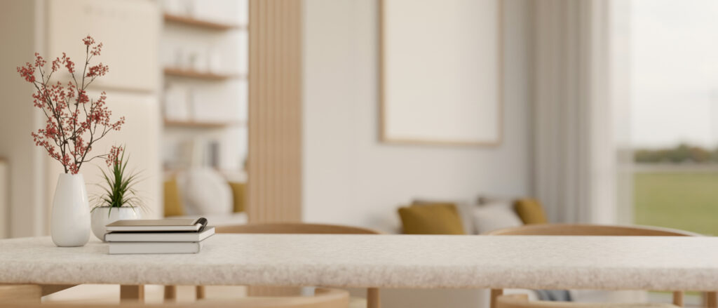 Modern dining table with a matte countertop finish, styled with a white vase holding red berries, a potted green plant, and minimalist white notebooks, set in a bright, airy interior with wooden accents and natural light