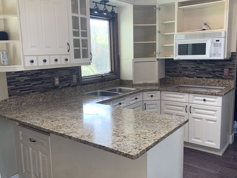 Kitchen with white cabinets and speckled granite countertops surrounding a corner sink