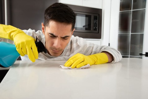 Person cleaning stains from a white quartz countertop in a modern kitchen